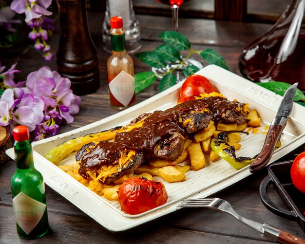 Filetes de cordero con salsa servida con papas fritas y vegetales ahumados