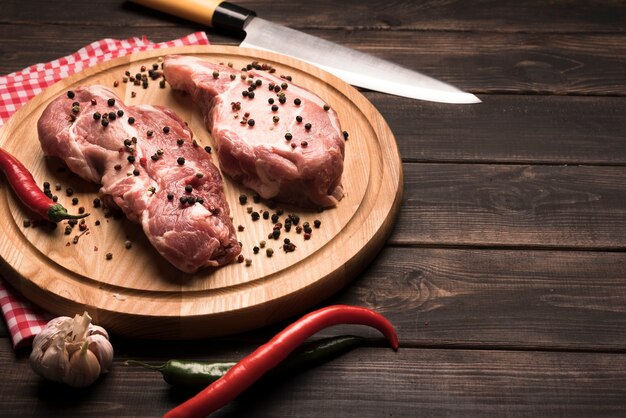 Filetes crudos de alto ángulo sobre tabla de madera con pimientos