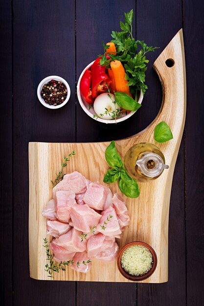 Filetes de pechuga de pollo cruda en tabla de cortar de madera con hierbas y especias. Vista superior