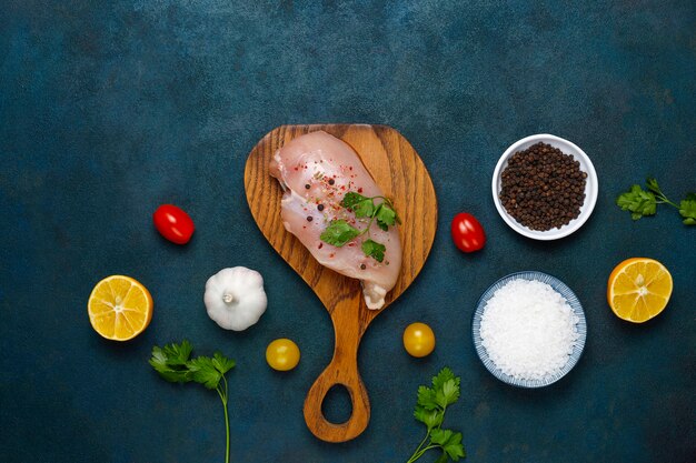 Filetes de pechuga de pollo cruda en tabla de cortar de madera con hierbas y especias vista superior.