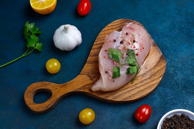 Filetes de pechuga de pollo cruda en tabla de cortar de madera con hierbas y especias vista superior.