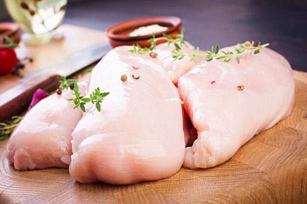 Filetes de pechuga de pollo cruda en tabla de cortar de madera con hierbas y especias.