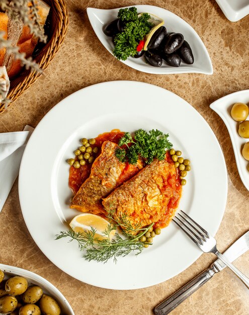 Filetes de pescado en salsa de tomate servidos con guisantes limón y hierbas