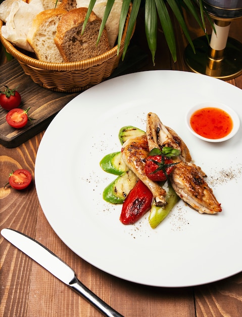 Filetes de pollo a la parrilla, asados y verduras en un plato blanco con salsa