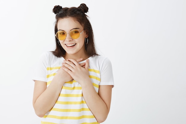 Foto gratuita filmación en interiores de elegante joven posando con gafas de sol contra la pared blanca