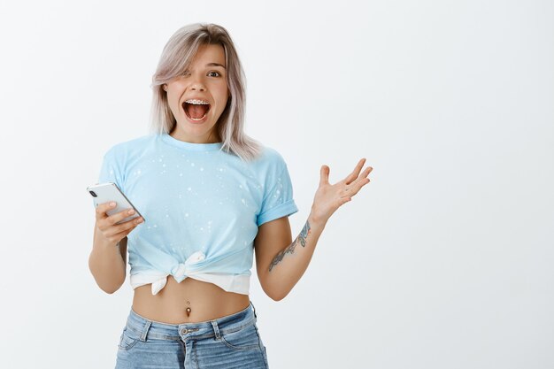 Filmación en interiores de feliz chica rubia posando en el estudio con su teléfono