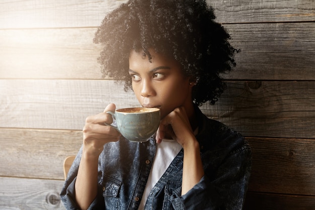 Filmación en interiores de hermosa mujer afroamericana con peinado afro sosteniendo taza grande