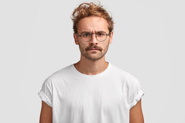 Filmación en interiores de hombre serio con expresión gruñona, descontento con vecinos ruidosos, vestido con camiseta blanca informal y gafas, plantea interiores