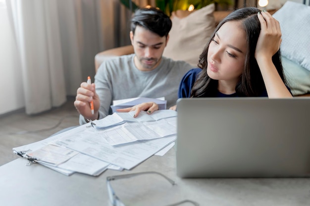 Finanzas domésticas esposo y esposa discutiendo el recibo de la factura en papel junto con el estrés y la sensación de confusión con muchos problemas y deudas en el interior del hogar