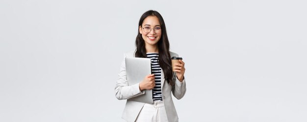 Finanzas empresariales y empleo concepto de emprendedoras exitosas Mujer de negocios guapa y segura en gafas y traje bebiendo café para llevar y llevar una computadora portátil de trabajo