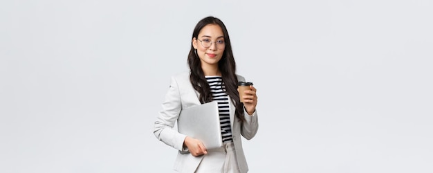 Finanzas empresariales y empleo concepto de emprendedoras exitosas Mujer de negocios guapa y segura en gafas y traje bebiendo café para llevar y llevar una computadora portátil de trabajo