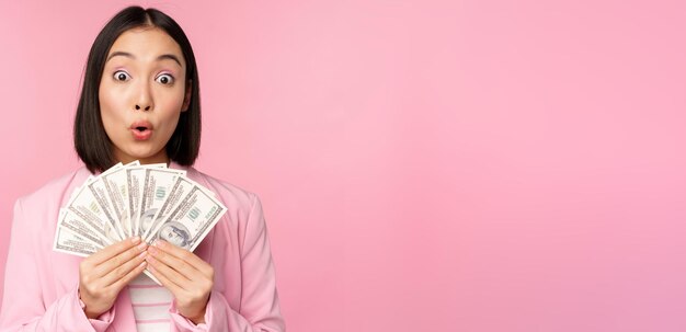 Finanzas microcrédito y concepto de personas Feliz empresaria asiática sonriente mostrando dólares dinero de pie en traje contra fondo rosa