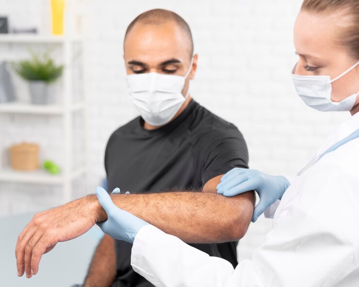 Foto gratuito fisioterapeuta femenina con máscara médica comprobando el codo del hombre
