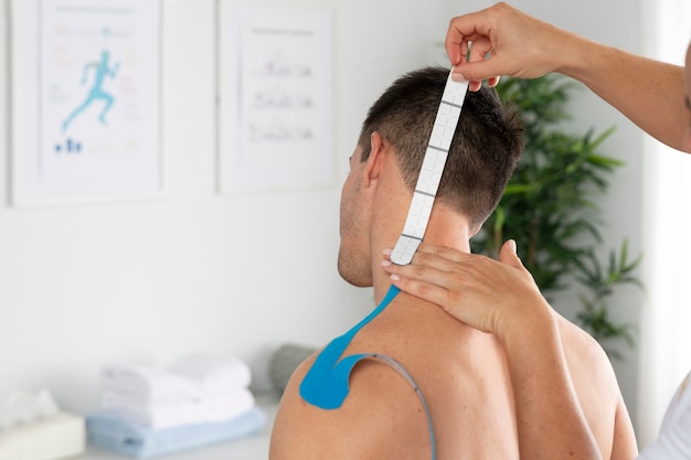 Fisioterapeuta femenino aplicando vendaje médico elástico al paciente masculino