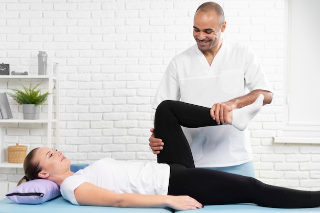 Foto gratuita fisioterapeuta masculino comprobando la flexibilidad de la pierna de la mujer