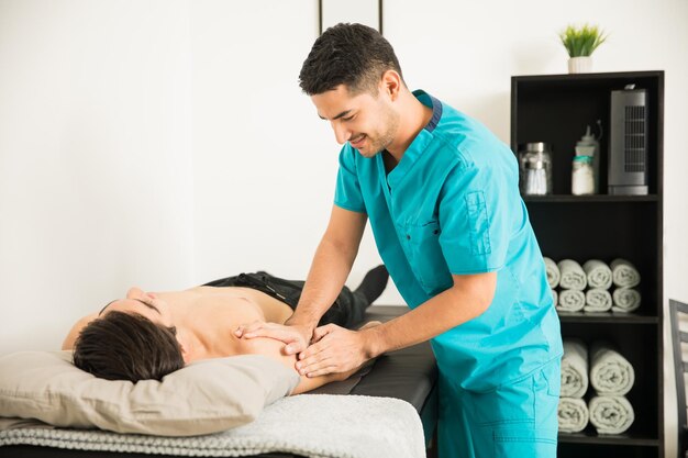 Fisioterapeuta masculino masajeando el hombro lesionado del atleta masculino en el hospital