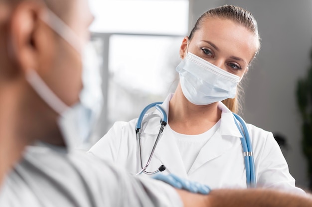 Foto gratuita fisioterapeuta mujer con máscara médica examinando al hombre