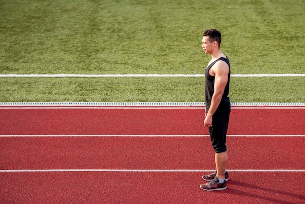 Fitness joven corredor masculino de pie en la pista roja