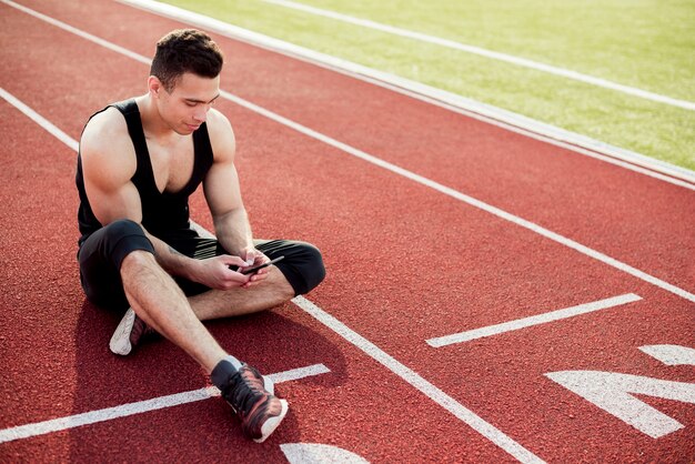 Fitness joven usando el teléfono móvil mientras está sentado en la pista de carreras