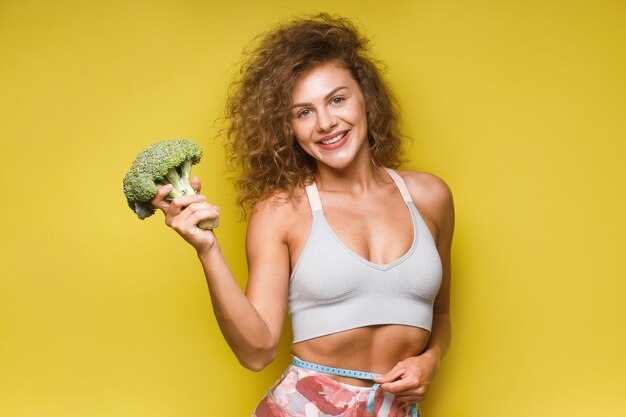 Fitness mujer deportiva recomienda una nutrición adecuada con brócoli grande en amarillo