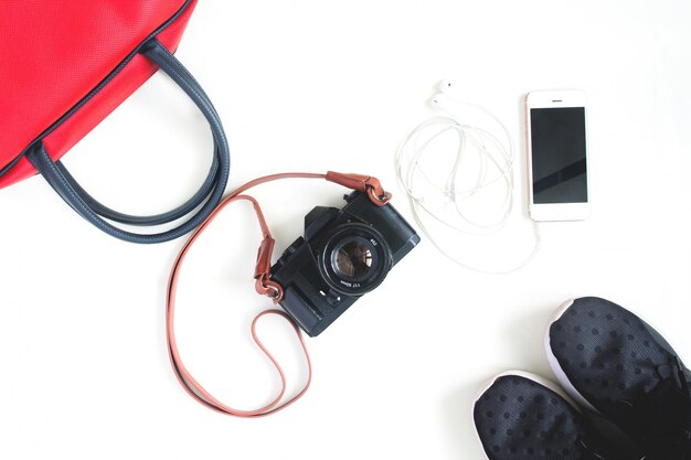 Flat lay de artículos de viaje con cámara de película, smartphone, bolso de mano rojo y zapatillas de deporte