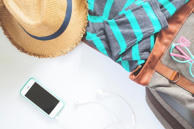 Flat lay ropa femenina y accesorios collage con camiseta, gafas de moda, sombrero con teléfono móvil y auriculares sobre fondo blanco.