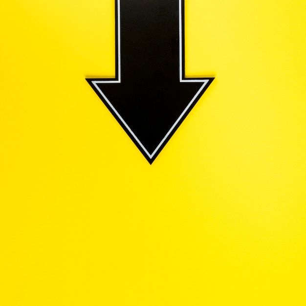 Flecha negra plana hacia abajo sobre fondo amarillo con espacio de copia