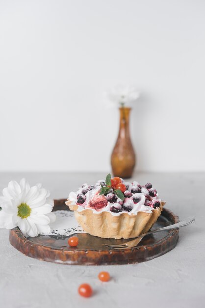 Flor blanca y deliciosas mini tartas con bayas frescas en bandeja de madera para servir