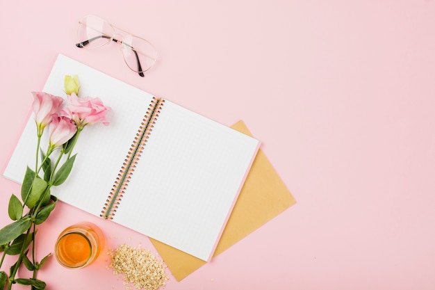Flor en un cuaderno abierto; los anteojos; jarra de jugo y muesli en fondo rosado