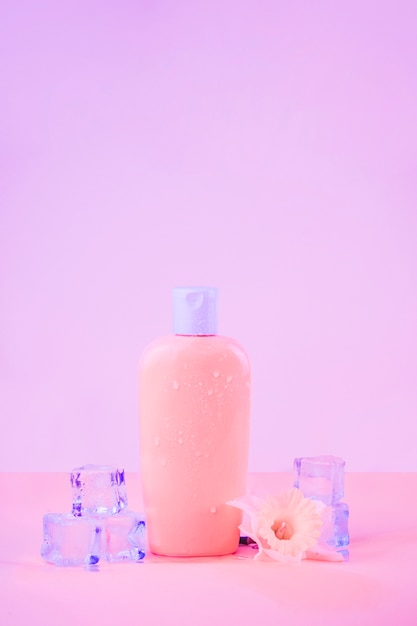 Flor con cubos de hielo de cristal con frasco de protección solar sobre fondo rosa