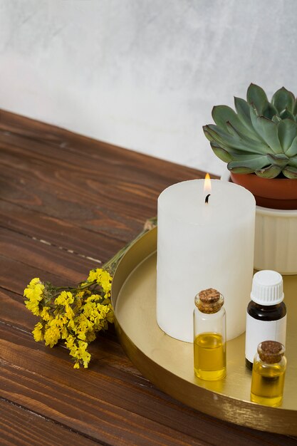 Flor de limonio con una vela grande e iluminada blanca y una botella de aceite esencial en el escritorio de madera