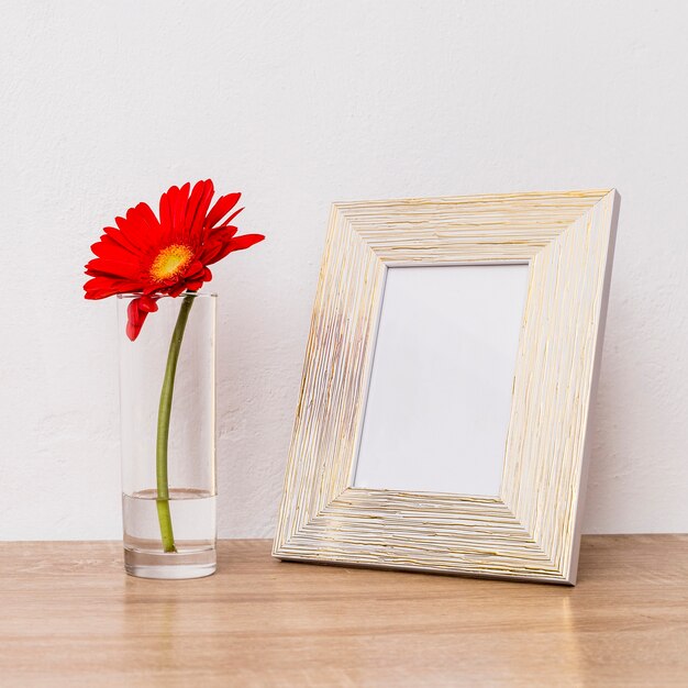 Flor roja en vidrio y marco de fotos en mesa