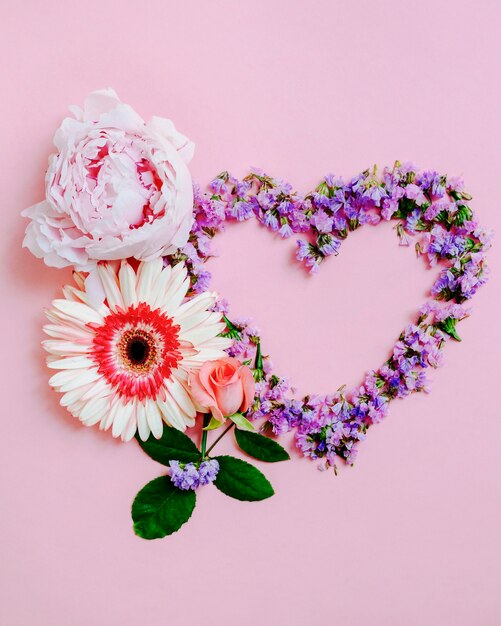 Flor de rosa, gerbera y peonía con forma de corazón sobre fondo rosa