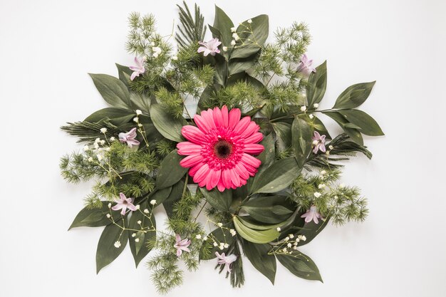 Flor rosa gerbera con ramas de plantas en mesa