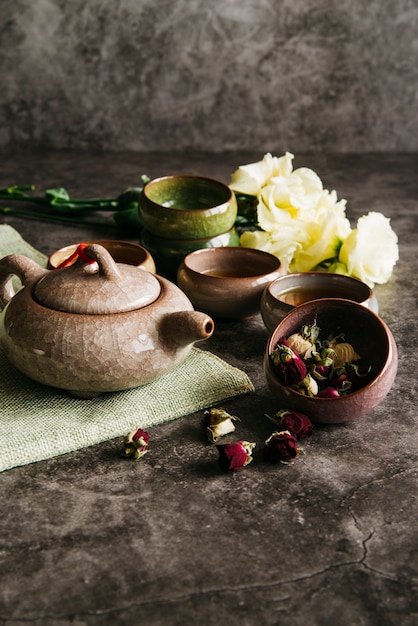 Flor de rosa seca con tetera; tazas de té y ramo de rosas sobre fondo de hormigón