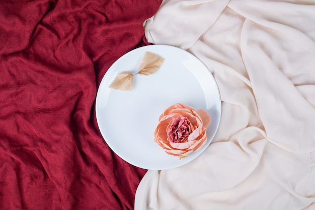 Flor única en plato blanco con manteles rojos y rosas.