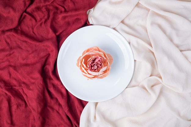 Flor única en plato blanco con manteles rojos y rosas.