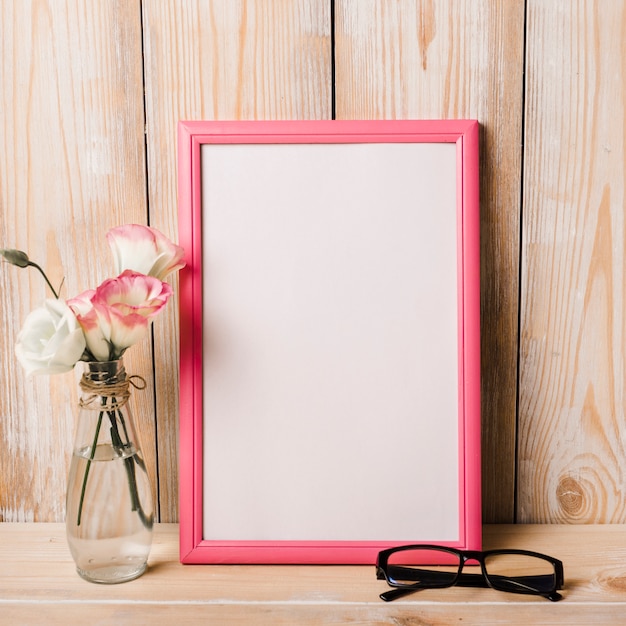 Foto gratuita florero y gafas cerca del marco blanco sobre el escritorio.