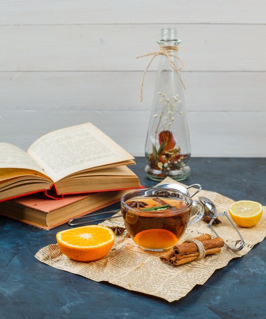 Florero y una taza de té con periódico, canela, naranja y un colador de té