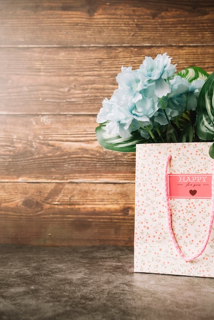 Flores artificiales en la bolsa de regalo de papel con fondo de madera.