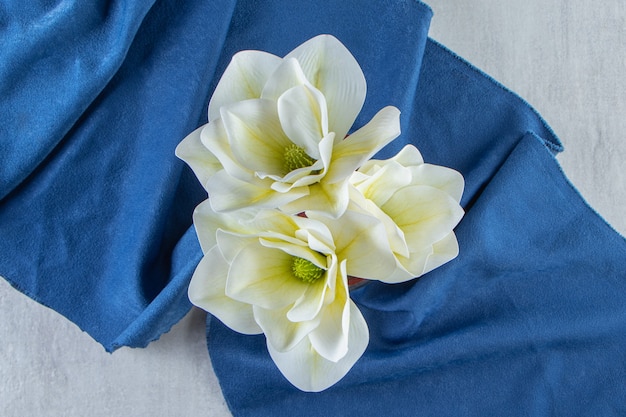 Flores blancas frescas en un vaso sobre un trozo de tela, sobre la mesa blanca.