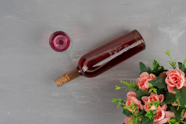 Flores, botella y copa de vino en superficie gris