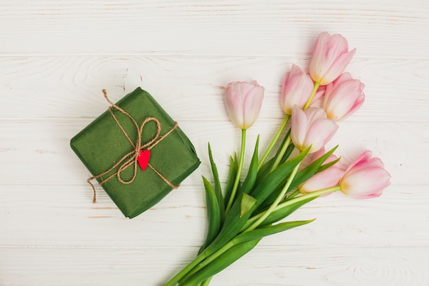 Flores y caja de regalo en mesa de madera blanca.