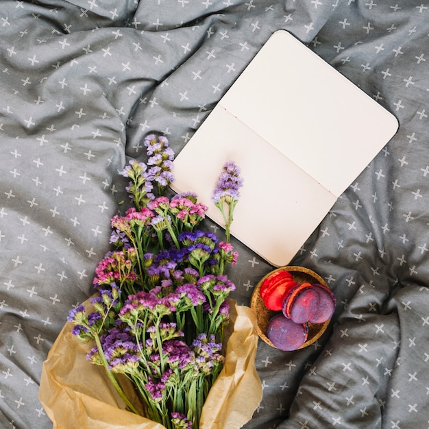 Flores cerca de macarrones y cuaderno en la cama