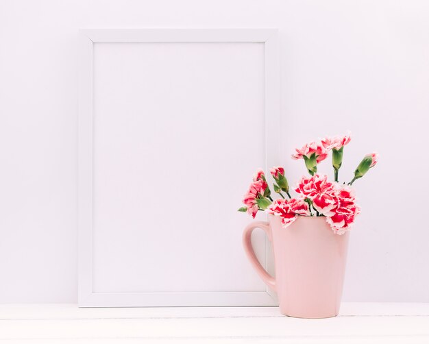 Flores de clavel en florero con marco de fotos vacío en mesa