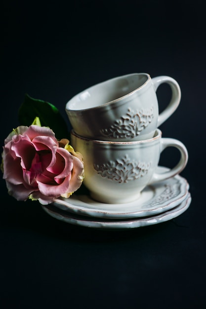 Flores de color rosa se encuentran en el plato por dos tazas de porcelana