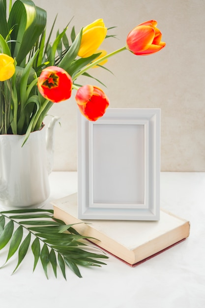 Foto gratuita flores en florero y marco de fotos colocados en una mesa cerca de la pared