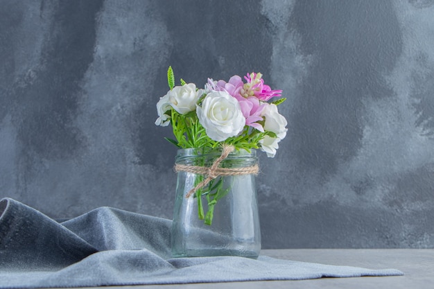 Flores en un frasco sobre un trozo de tela, sobre la mesa blanca.