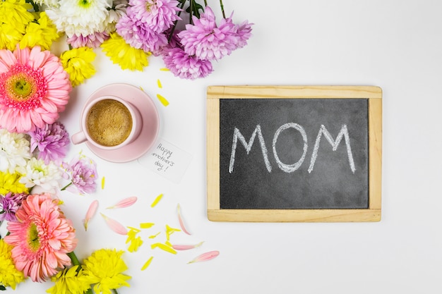 Foto gratuita flores frescas cerca de la taza de bebida, pizarra con palabras de mamá y pétalos