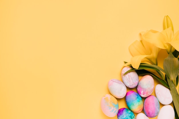 Flores frescas del lirio con los huevos de pascua coloridos en la esquina del fondo amarillo